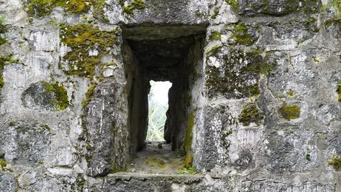 Stone wall with moss-covered opening revealing greenery beyond 스톡 사진