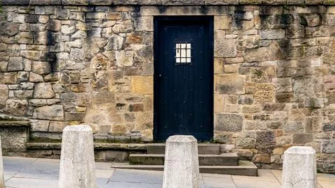 Stone wall with an old black massive wooden door. Stock Photos