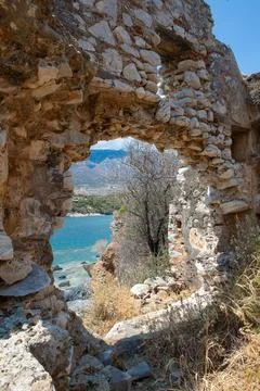 Stone wall opening framing view of turquoise water and mountain 스톡 사진