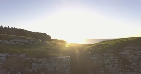 Stone wall over looking green landscape and sea at sunset Stock Footage 106192703
