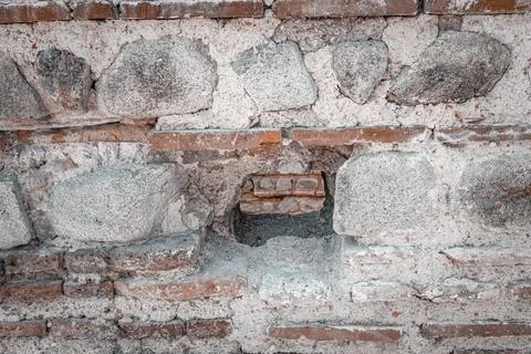 Stone wall with visible brickwork and a small opening in historic location Stock Photos