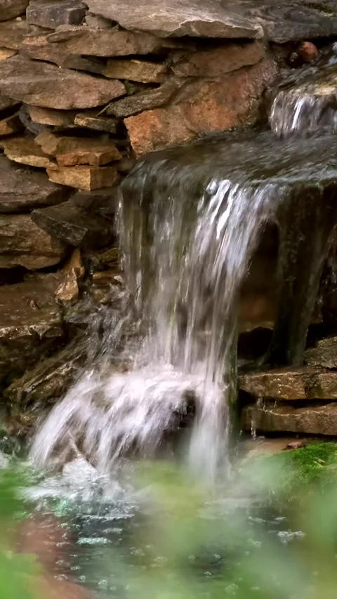 Stone wall with a waterfall in the garden. Artificial decorative waterfall from Video stock 285484363