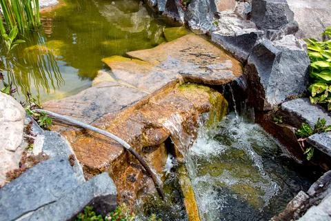 Stone waterfall in an artificial pond with flow water in the backyard. Stock Photos