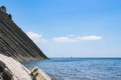 Stone wild beach, huge cliffs with pine trees and bright blue sky with clouds Photos