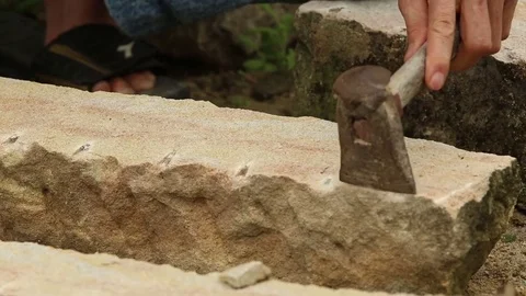 A stonecutter or stonemason is profiling the cut of a stone with a wide chisel. Stock Footage 77314333