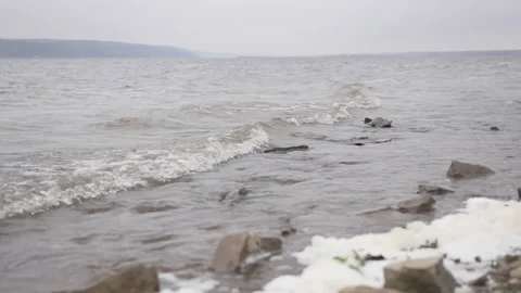 Stones line edge of river as white-capped waves lap shore Stock-Footage 306458998