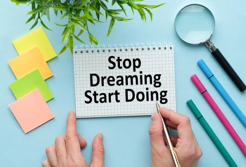 Stop Dreaming Start Doing text on notebook writing hands on blue office desk Stock Photos