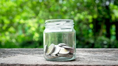 Stop motion animation coin into a clear glass jar on wooden desk Stock Footage 161139641