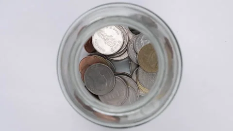 Stop motion animation coin into a clear glass jar on white table. Stock Footage 247113103