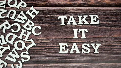 Stop motion animation of white letters on wooden background. Take it easy slogan Stock Footage 160209192