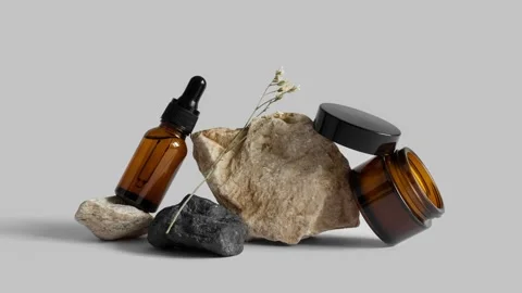 Stop motion loop of glass pipette bottle, jar of cream, flower branch on rocks Video stock 154572775