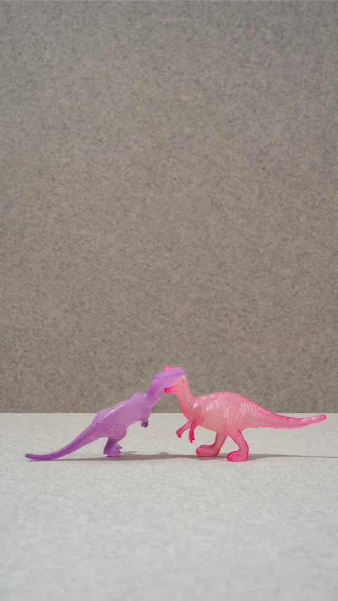 A stop motion scene featuring two toy dinosaurs, one purple and one pink, Video stock 330376383