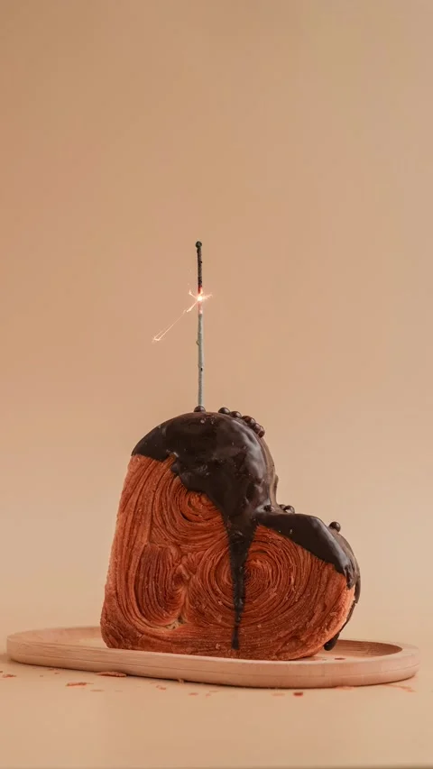 Stop motion Shiny candle sparkler Heart shaped dark chocolate croissant on beige Stock Footage 319428659