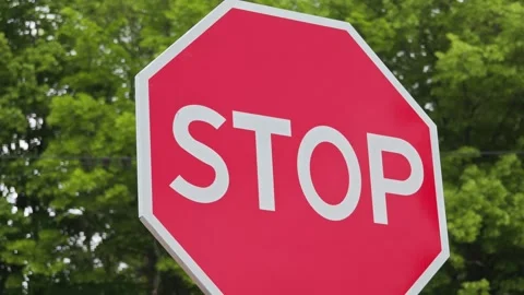 Stop sign gently moving in the wind with green trees background Vidéo 311025515