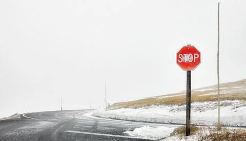 Stop sign at a mountain roads intersection during blizzard, selective focus,  Stock Photos