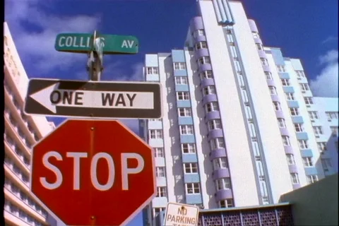 A stop sign, one way sign and a street sign stands in front of an art deco Stock Footage