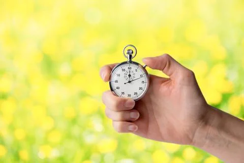 Stopwatch hold in hand, button pressed; flower background spring concept Stock Photos