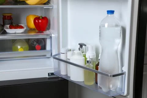 Storage of cosmetics and water in refrigerator door bin next to groceries Stock Photos