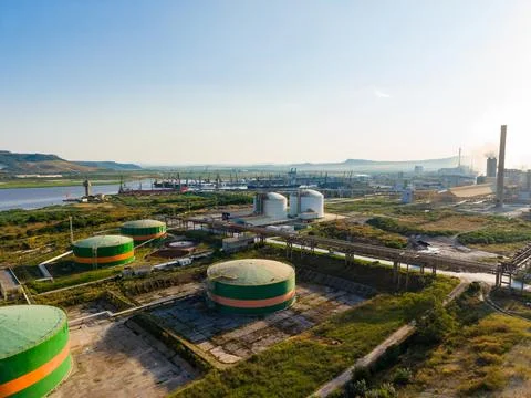 Storage tanks are present in the foreground, with factories and cranes visibl Stockfoto's