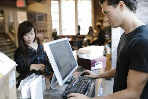 Store assistant using computer and serving woman at counter Foto stock