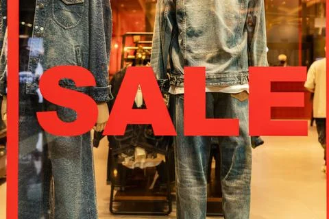 The store window features denim outfits on mannequins with a bright sale si.. Stock Photos