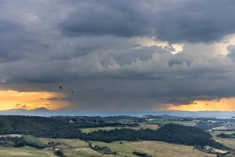 Storm cloud building up from afar during sunset over agricultural landscape in Stock Photos