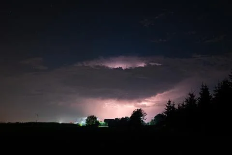 Storm cloud is illuminated by lightning under a starry sky. Stock Photos