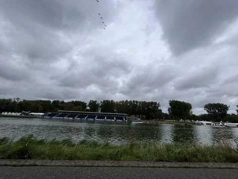 Storm clouds gather above riverside rowing venue with wide water channel Photos