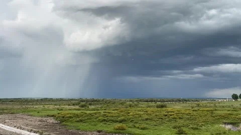 Storm Clouds Hover Over Green Fields with Visible Rain in Xinjiang China Stock Footage 339172128