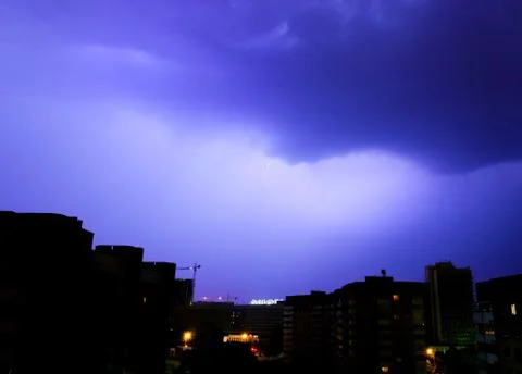 Storm clouds illuminated by distant flashes over the city Stock Photos