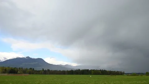 Storm clouds moving above green field and majestic snowy mountains Stock Footage 190031089