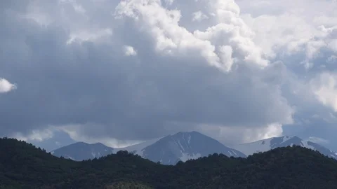 Storm clouds over snowcapped mountain peaks behind foothills. 動画素材 118775839