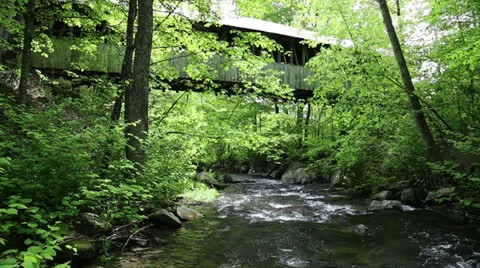 Storm swollen stream running under and covered bridge Stock Footage 24250039