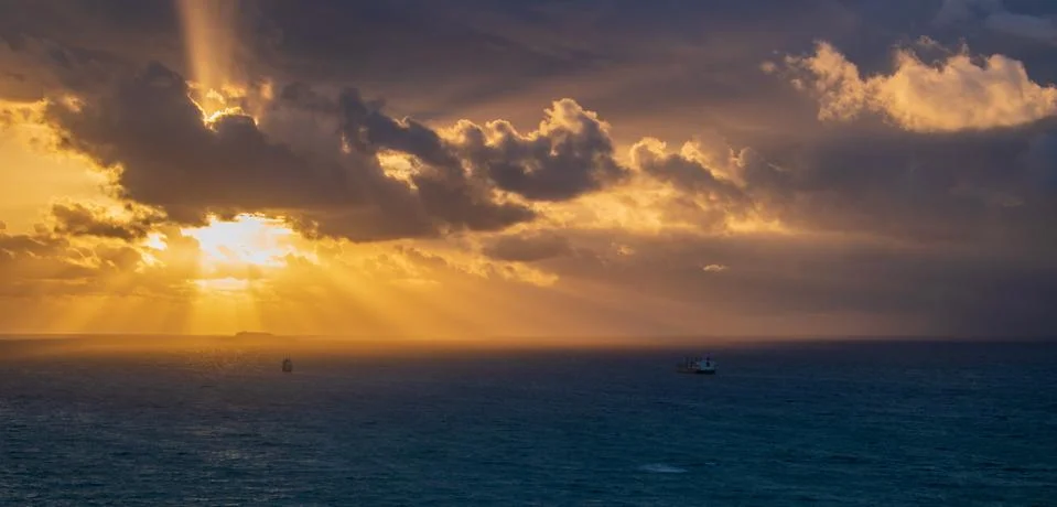 Storm with thick dark clouds approaching the coast at sunrise. Light beams ar Stock Photos