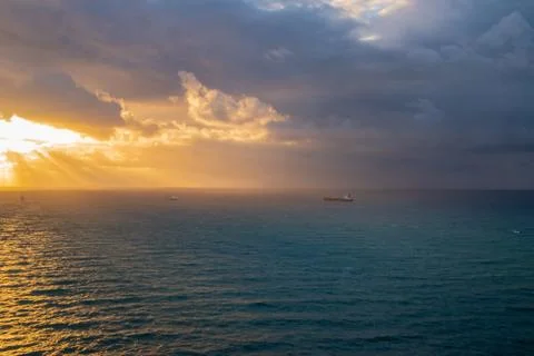 Storm with thick dark clouds approaching the coast at sunrise. Light beams ar Stock Photos