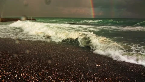 Storm waves roll over the pebble beach, with a breakwater and a double rainbow Stock Footage 218405594