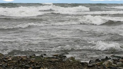 Storm waves roll onto the rocky shore of the evening lake. Stock Footage 290120036