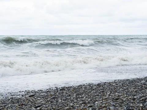 Storm waves on a stone beach in cloudy weather Stock Photos