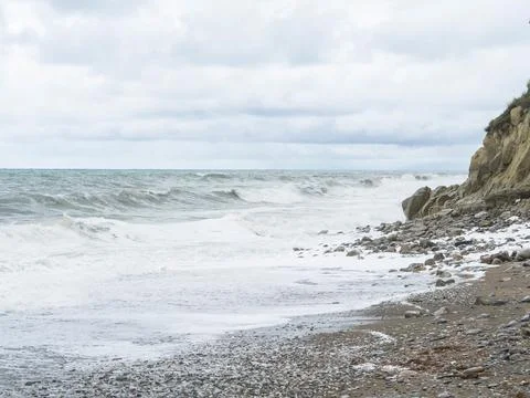 Storm waves on a stone beach in cloudy weather. Stock Photos