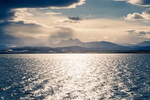 Stormclouds with sun shining through them above dramatic mountain range of Stock Photos