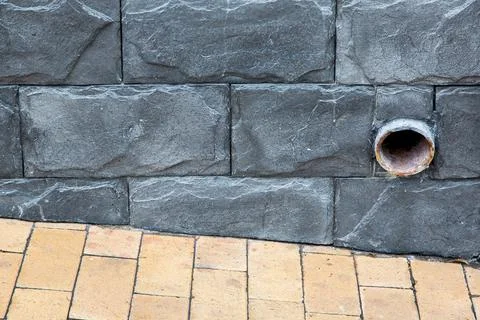 A stormwater pipe emerging from the dark gray tile wall on the building. Stock Photos