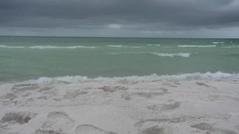 Stormy beach with footprints and rough ocean waves under an overcast sky Stock Footage 345689558