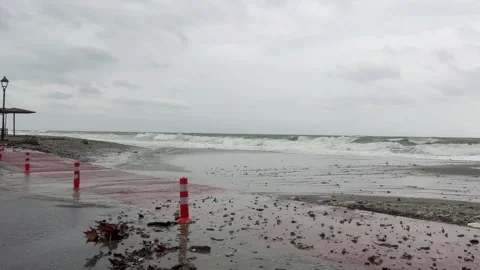Stormy beachside waves crashing against red pavement amid overcast skies Stock Footage 325520643