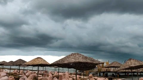 Stormy Grey Clouds Over Empty Beach with Straw Umbrellas and Calm Sea Stock Footage 330084455
