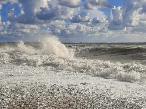 Stormy ocean waves breaking on a pebble beach under a cloudy sky Stock Photos
