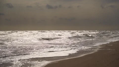 Stormy ocean waves crash on sandy shore under overcast skies. Wild, natural Stock Footage 261375914