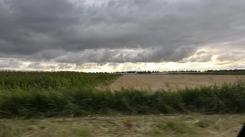Stormy rural landscape with dramatic clouds over green cornfield, harvested 库存照片
