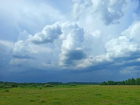 Stormy sky with dramatic clouds over green meadow landscape Stock Photos