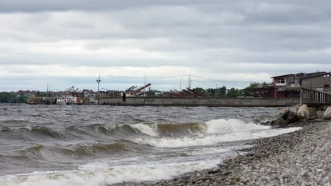 Stormy waves crashing on a pebble beach near a harbor Stock Footage 346051759