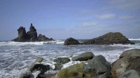 Stormy waves roll over the rocky shore. Black rocks of frozen magma stick out of Stock Footage 231497061